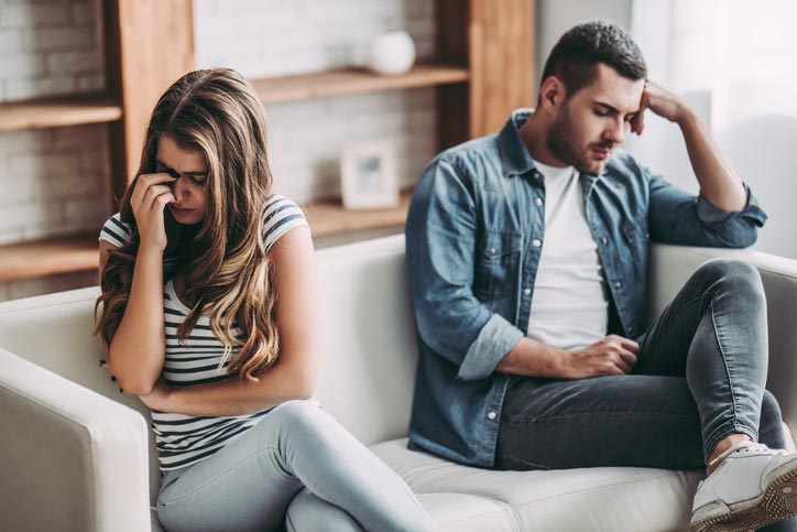 Couple sitting at a distance from each other on couch, appearing distraught